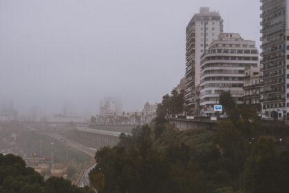 A misty cityscape featuring tall buildings lining an elevated road in a foggy urban environment.